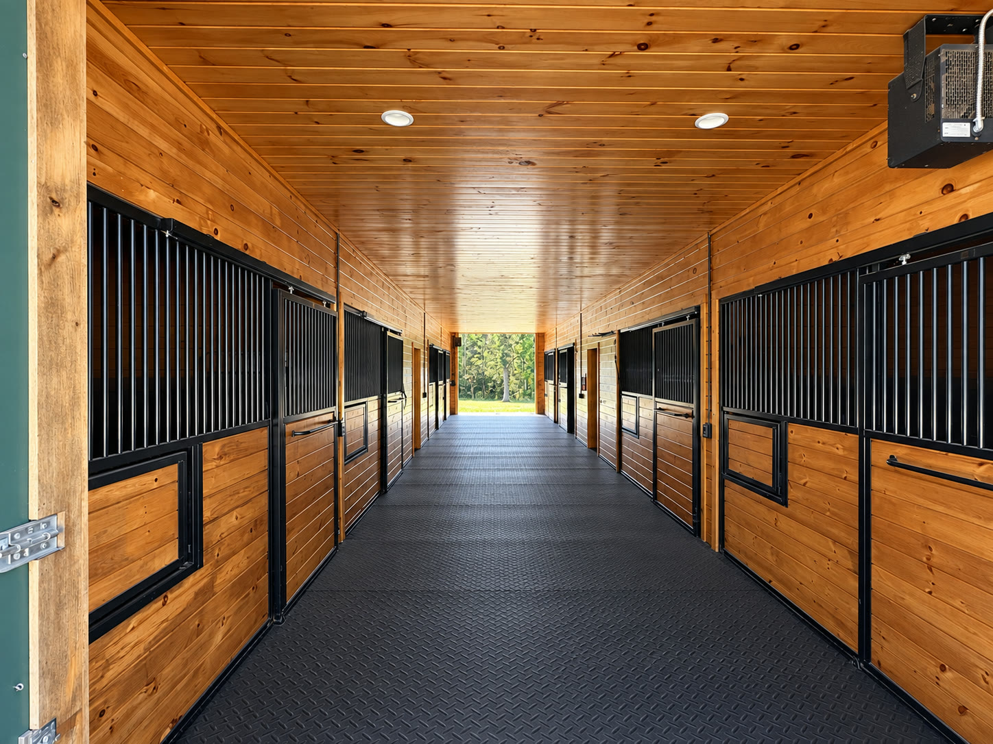 Stained wood barn aisle with horse stalls opening to a pasture